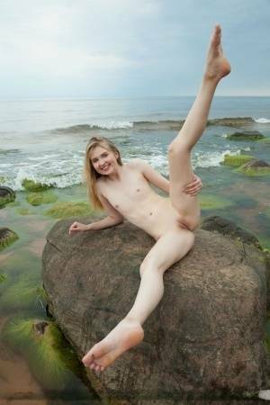 Slim teen Nimfa removes a black bikini to pose naked on seaside rocks on shefanatics.com