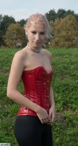 Collared girl Arienh Autumn models a red leather corset while in a field on shefanatics.com