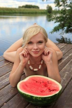 Beautiful blonde Feeona eats a watermelon while posing naked on lakeside dock on shefanatics.com